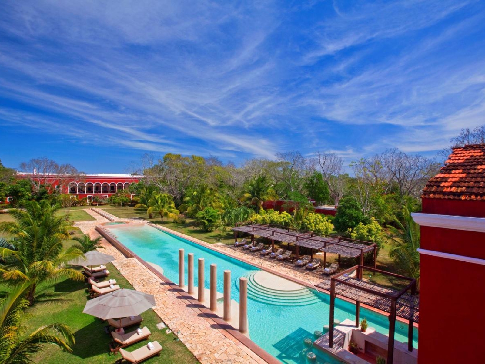 Hacienda roja con una larga alberca entre jardines tropicales de Yucatán